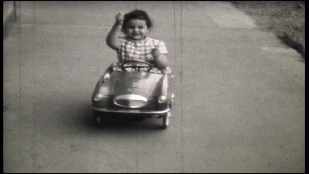 Funny child driving her toy car and laughing in 1966
